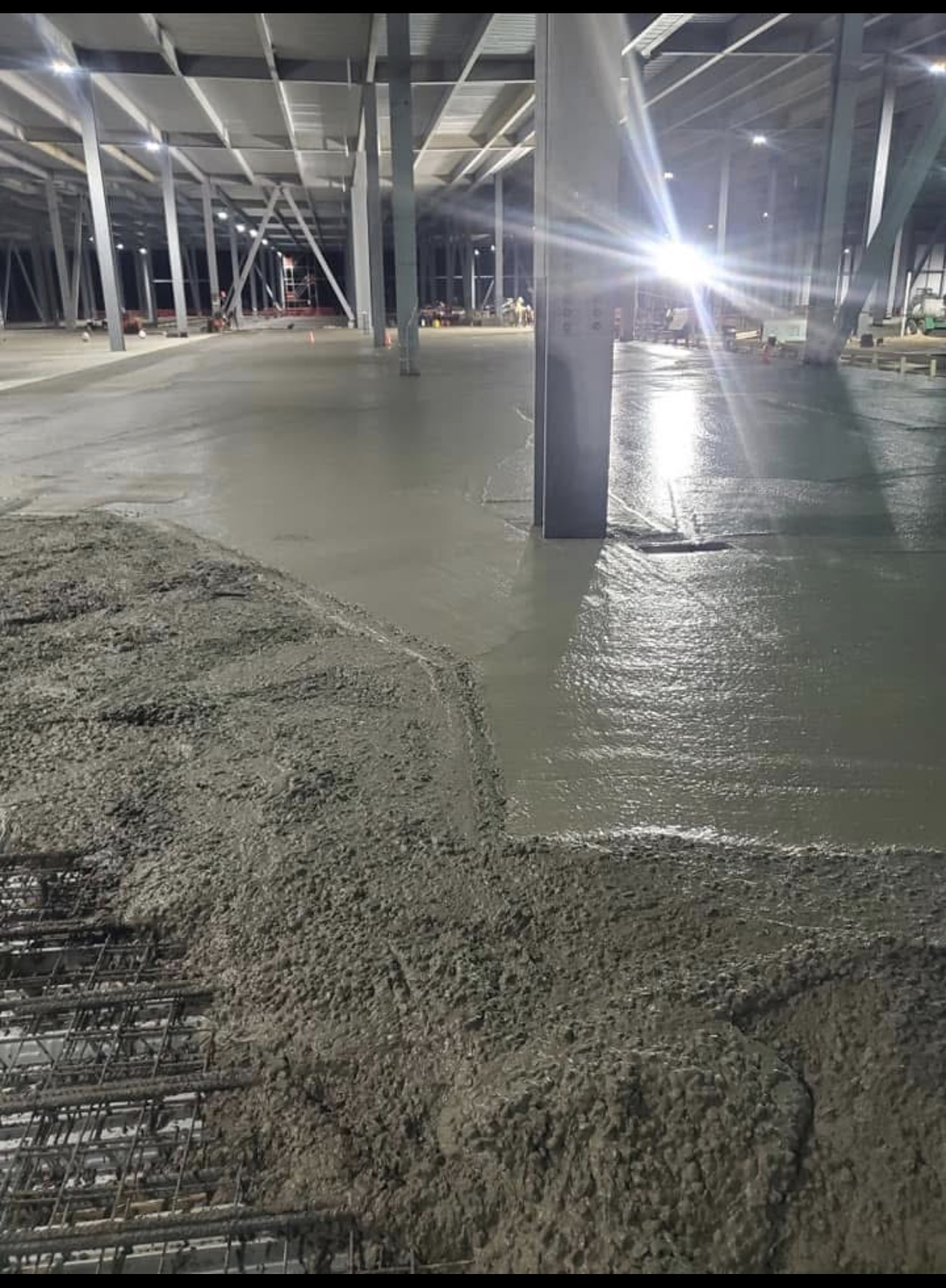 Freshly poured and floated concrete slab inside a large warehouse at night